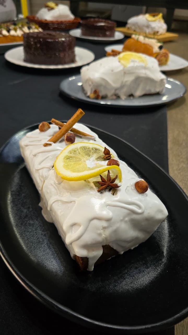 Panqué glaseado decorado con rodaja de limón, canela, avellanas y anís estrella sobre plato negro