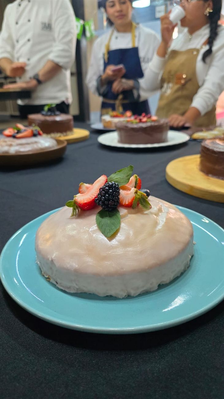 Pastel redondo con glaseado perlado decorado con fresas, zarzamora y albahaca sobre plato azul