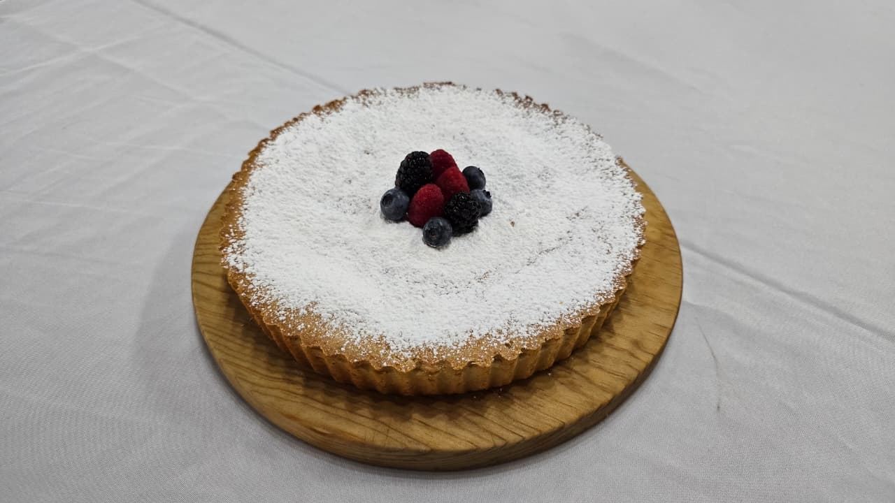 Tarta de almendra nevada con azúcar glass y frutos rojos al centro, sobre base de madera